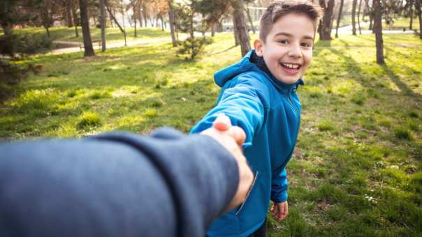 jongen in park die hand van ouder vasthoudt