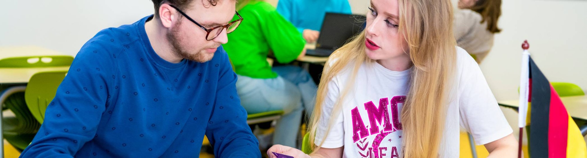 Twee studenten zitten in grote grijze stoelen te overleggen met twee medestudenten.