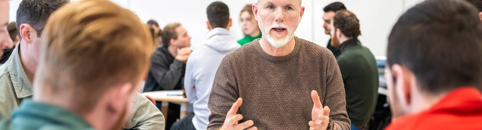 Docent zit bij studenten aan tafel en is aan het woord.