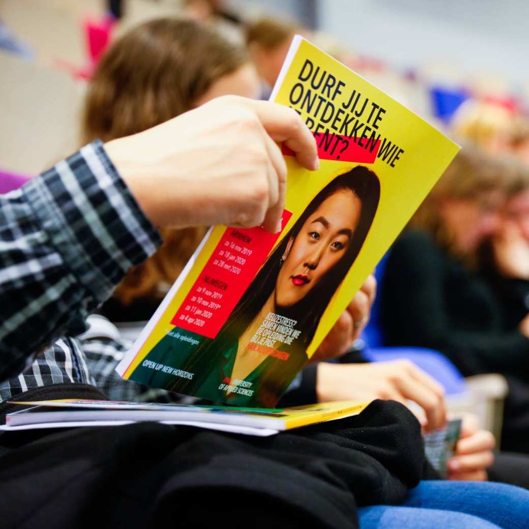 Bezoeker bladert door HAN magazine voltijd brochure in auditorium bezoekers op achtergrond