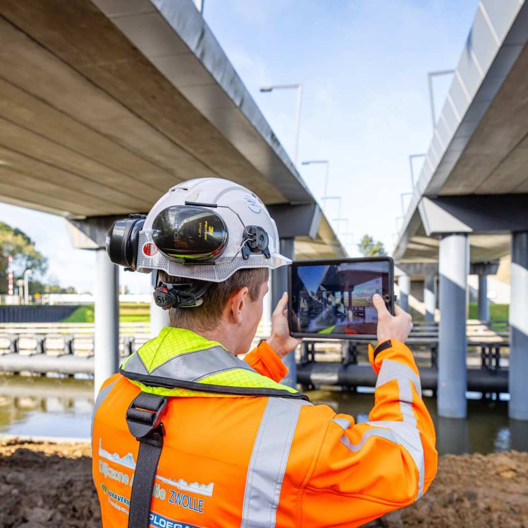 Man met veiligheidshelm en oranje werkjas fotografeert van onderen twee viaducten in aanbouw