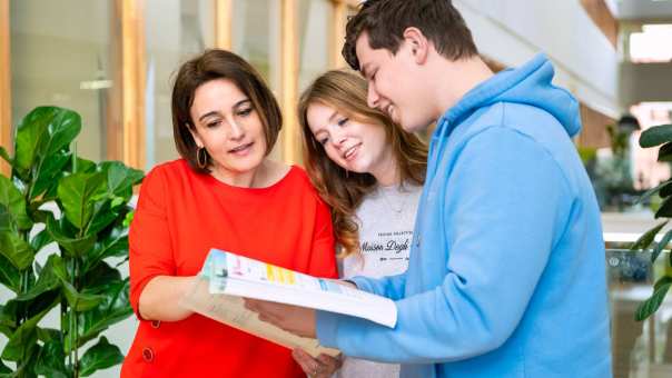 Docent staat met haar twee studenten in een boek te kijken.