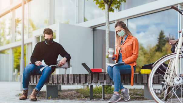 Studenten buiten op bankje met mondkapjes op. Social distancing. Anderhalve meter. Covid19. Corona.