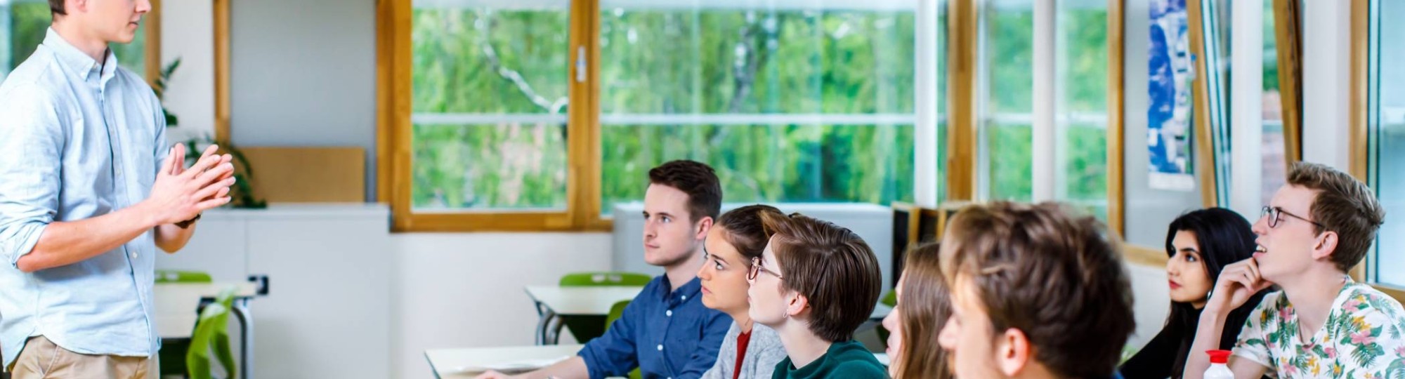 Jonge docent staat voor de klas en geeft les aan zijn groep studenten die aandachtig luisteren naar hem. 