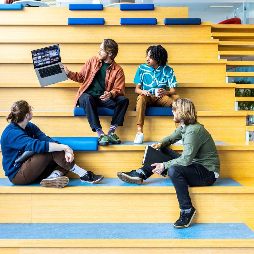 Docent CMD laat voorbeeld zien via zijn laptop aan studenten op de trap.