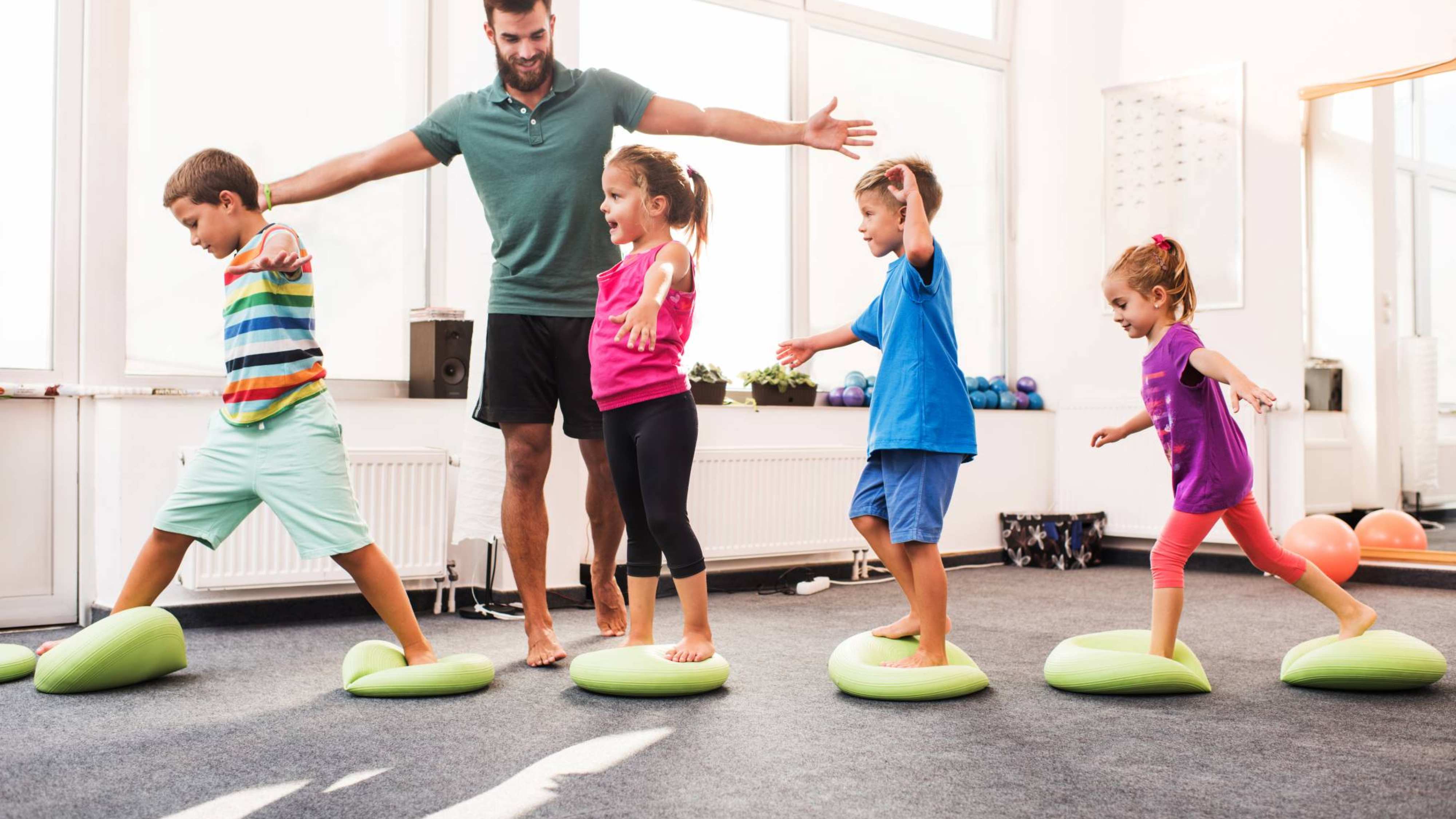 kinderen wandelen op pilates-ballen tijdens training op sportschool met mannelijke coach