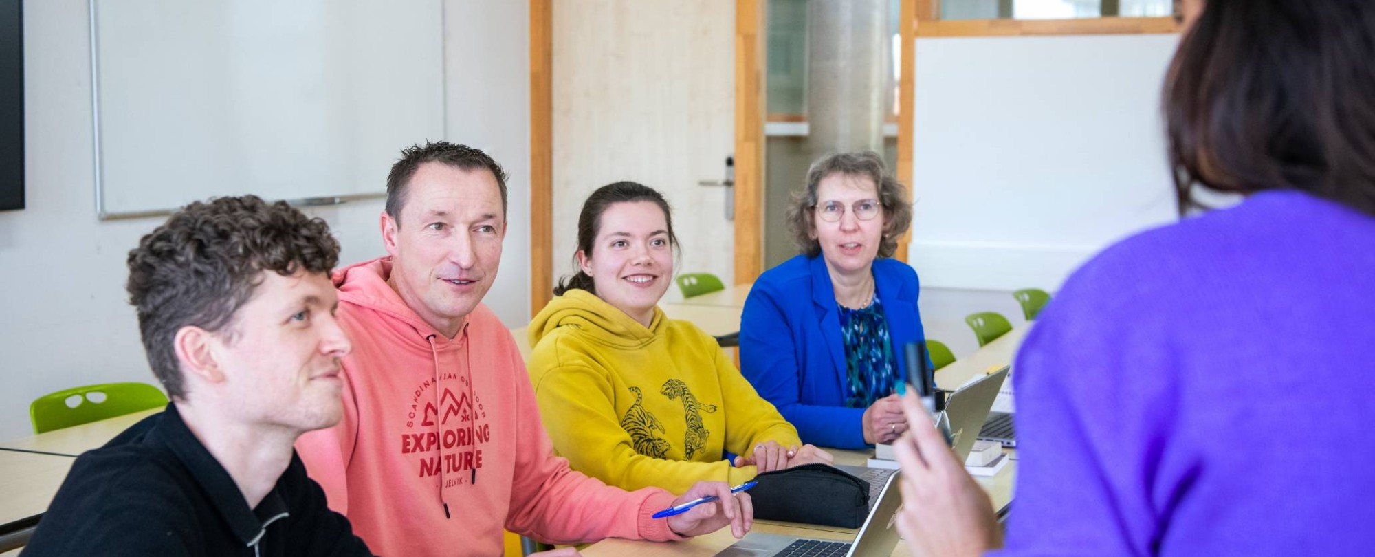 vier masterstudenten luisteren aandachtig naar een docent voor ze