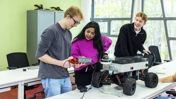 drie studenten werken tijdens de les aan een robotauto 