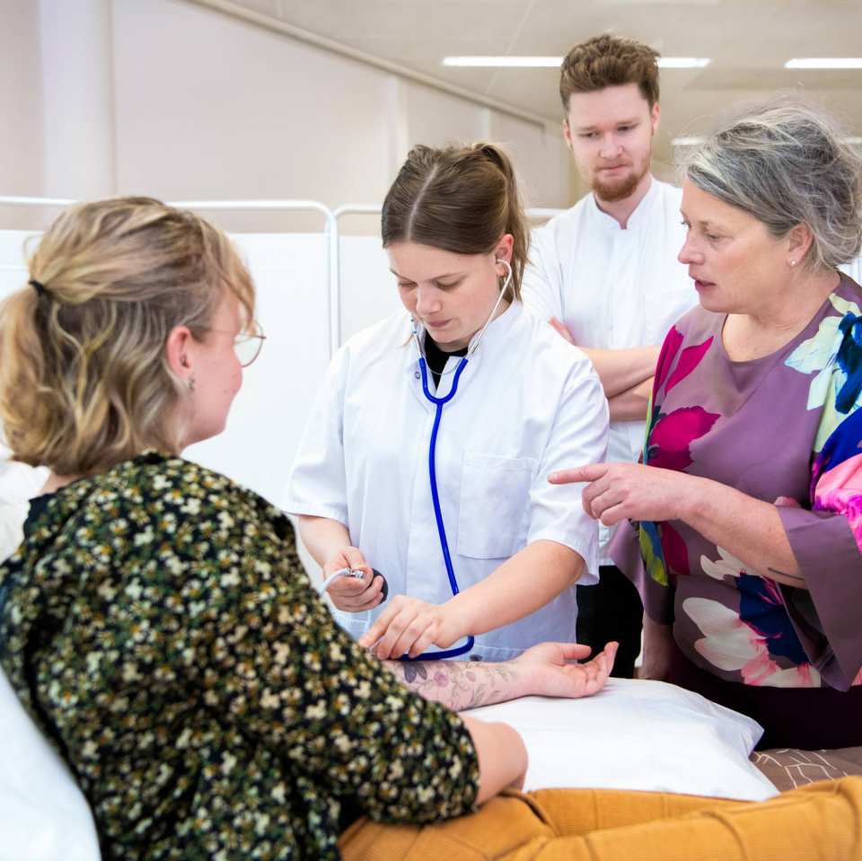 Docent geeft uitleg aan 3 studenten tijdens bloeddruk meten