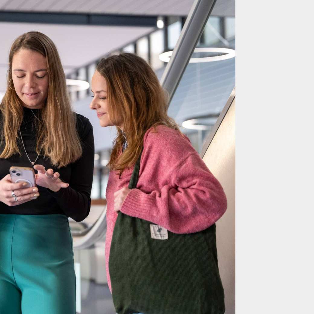 2 duale studenten kijken op een mobieltje in de hal.