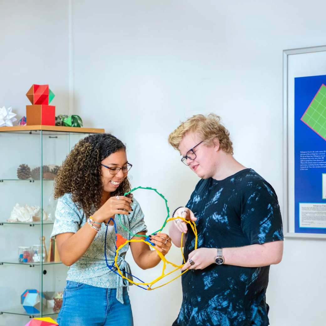 Docent houdt een wiskundig model van gekleurde potloden in de lucht en haar drie studenten kijken ernaar.