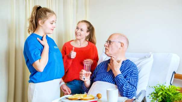 Studenten Logopedie staan bij bed client en geven uitleg