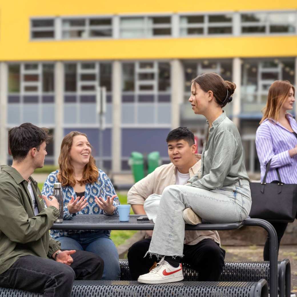 Groepje studenten zitten buiten aan de picknicktafel, op de campus Arnhem. 