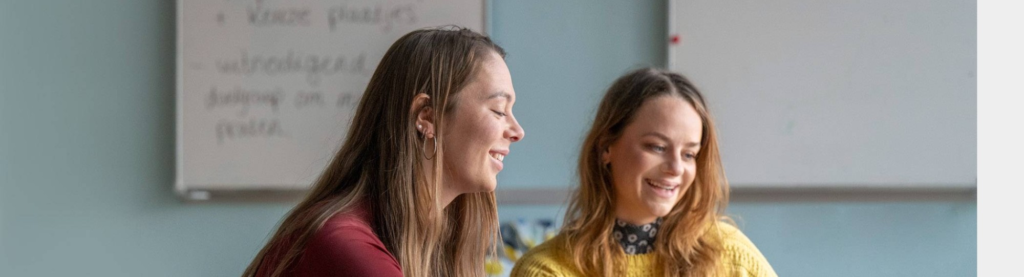 Twee deeltijdstudenten overleggen lachend met elkaar in de klas.