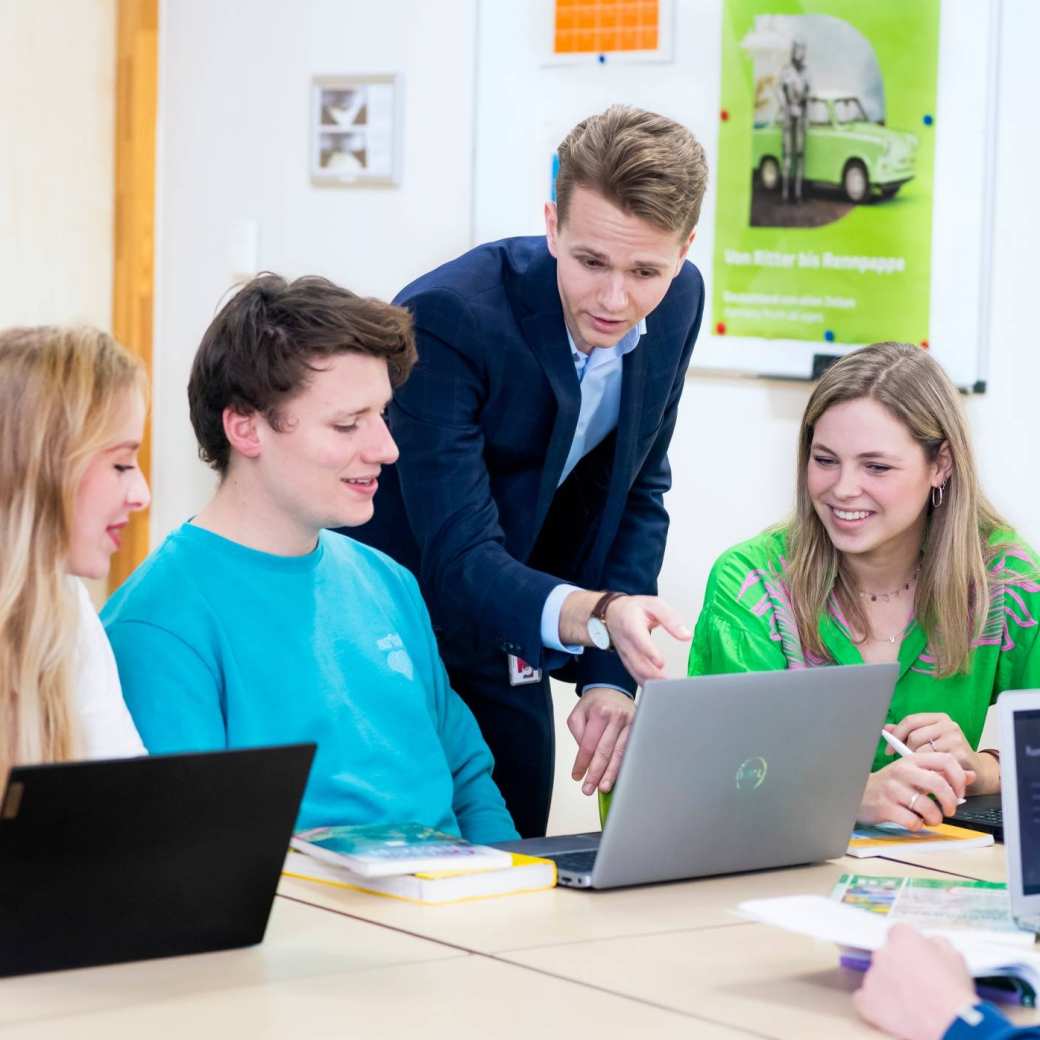 Docent legt drie studenten aan de tafel iets uit.