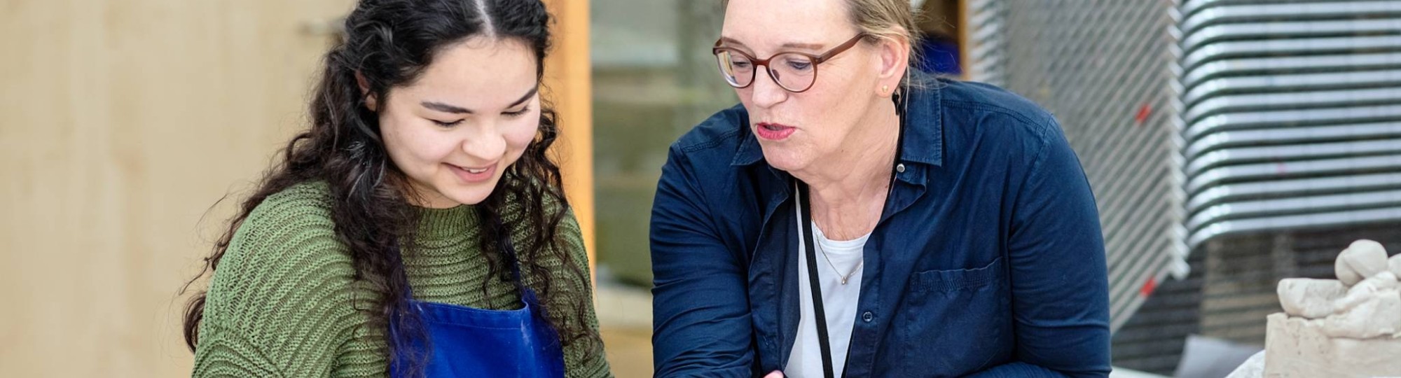 Fotoshoot maakdagen beeldende vorming 2022. Docent met studente tijdens les beeldende vorming. Helpt met kleien.