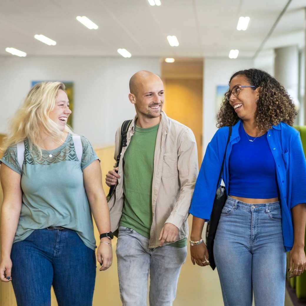 Twee studenten kijken naar de laptop waar de lerares naar wijst.