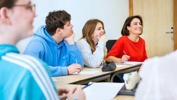 Studenten zitten op een rij en hun hoofd steunt op de handpalm. Ze kijken lachend en vragend.