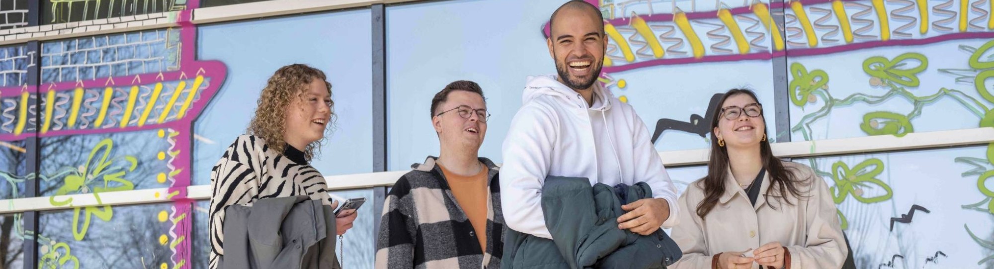 Groep student en een docent lachend voor een vrolijke wand