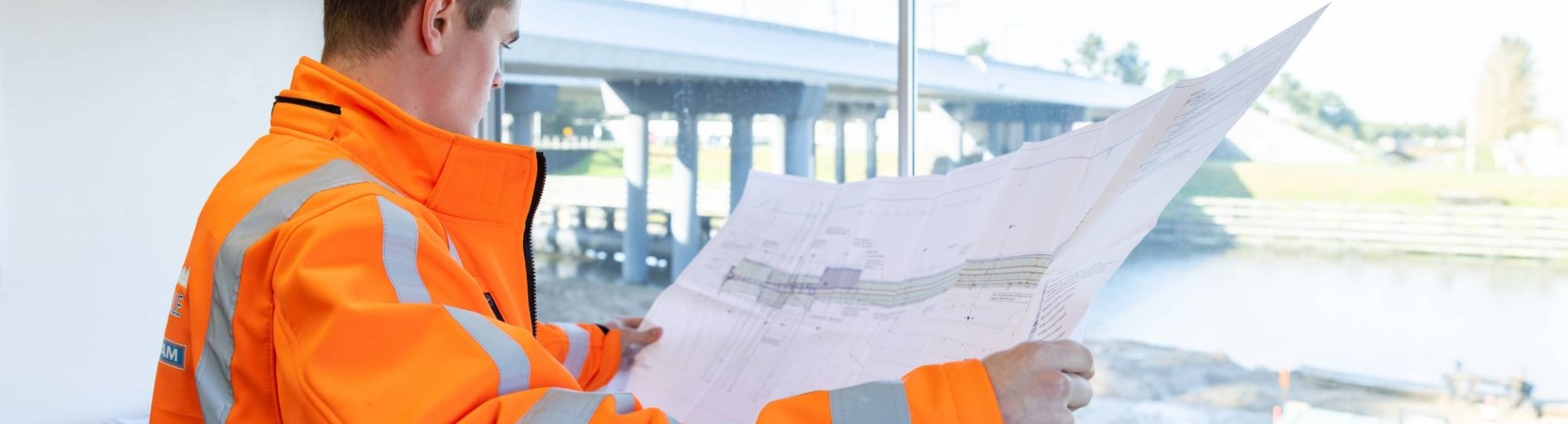 opzichter in de directiekeet kijkt met tekeningen in de hand uit over het bouwterrein