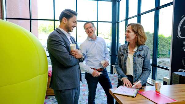 drie personen staan te praten en lachen met elkaar in een ruimte met glazen wanden