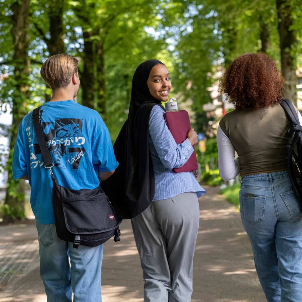 Studenten lopen buiten van K33 naar LvS10, pad bij bomen, campusterrein. 