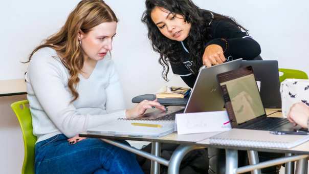 Twee studenten Leraar Engels kijken aandachtig naar de laptop en één student wijst naar het scherm.
