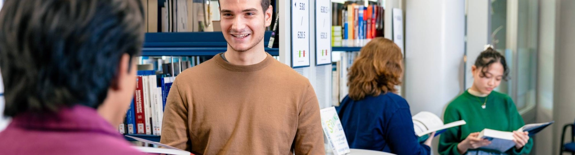 International students Diego, Andrei, Noa and Tam browsing through books in the library on the Arnhem campus of HAN University of Applied Sciences.