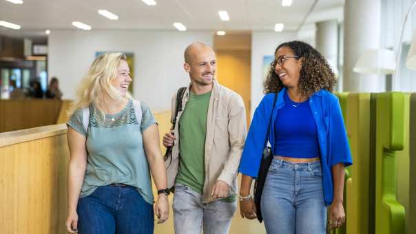 Drie studenten Leraar Wiskunde lopen lachend naast elkaar op de gang in de school