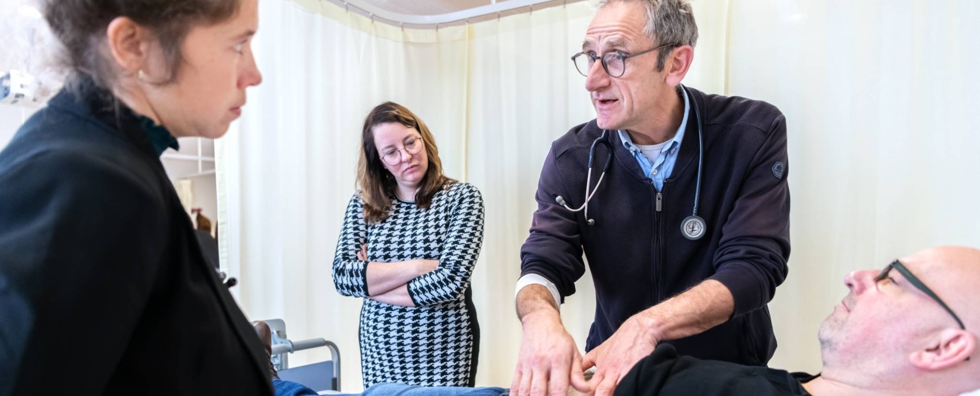 docent van de han master physician assistant geeft uitleg aan 2 studenten over een medische handeling bij een patient op de onderzoeksbank