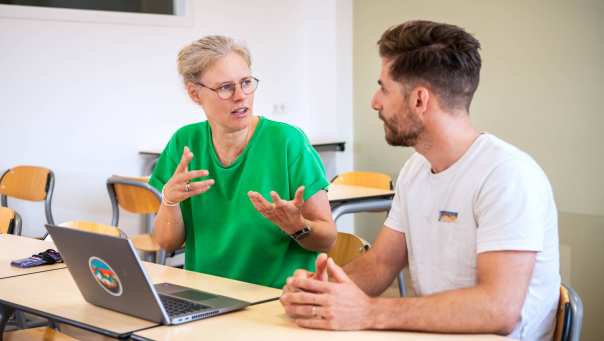 Docent geeft uitleg aan student aan tafel achter laptop tijdens les PMT deeltijd