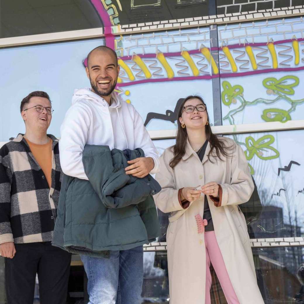 Groep student en een docent lachend voor een vrolijke wand