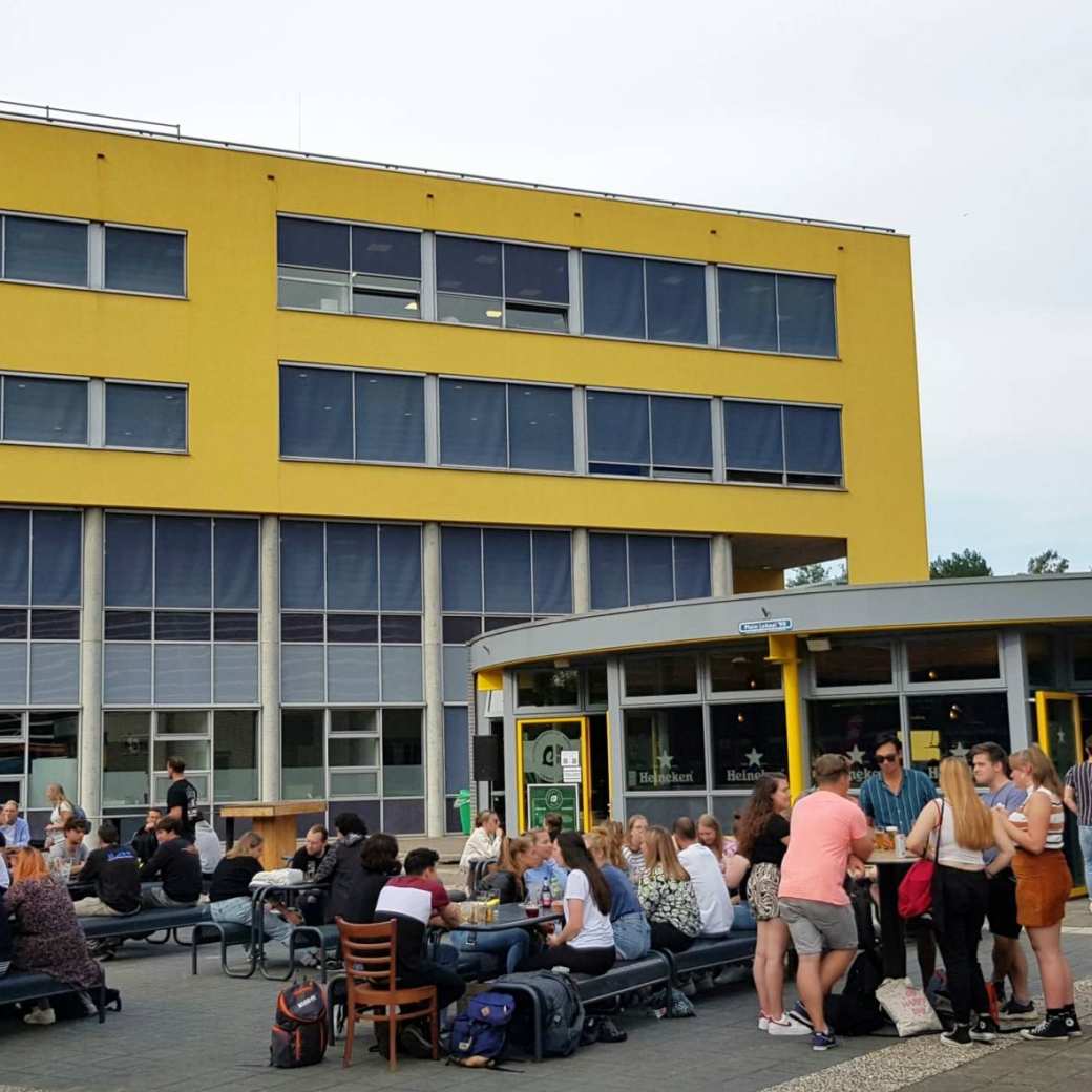 Studenten komen na de lessen samen bij Lokaal 99 om iets te drinken. Op de achtergrond het onderwijsgebouw van Engineering en Automotive.