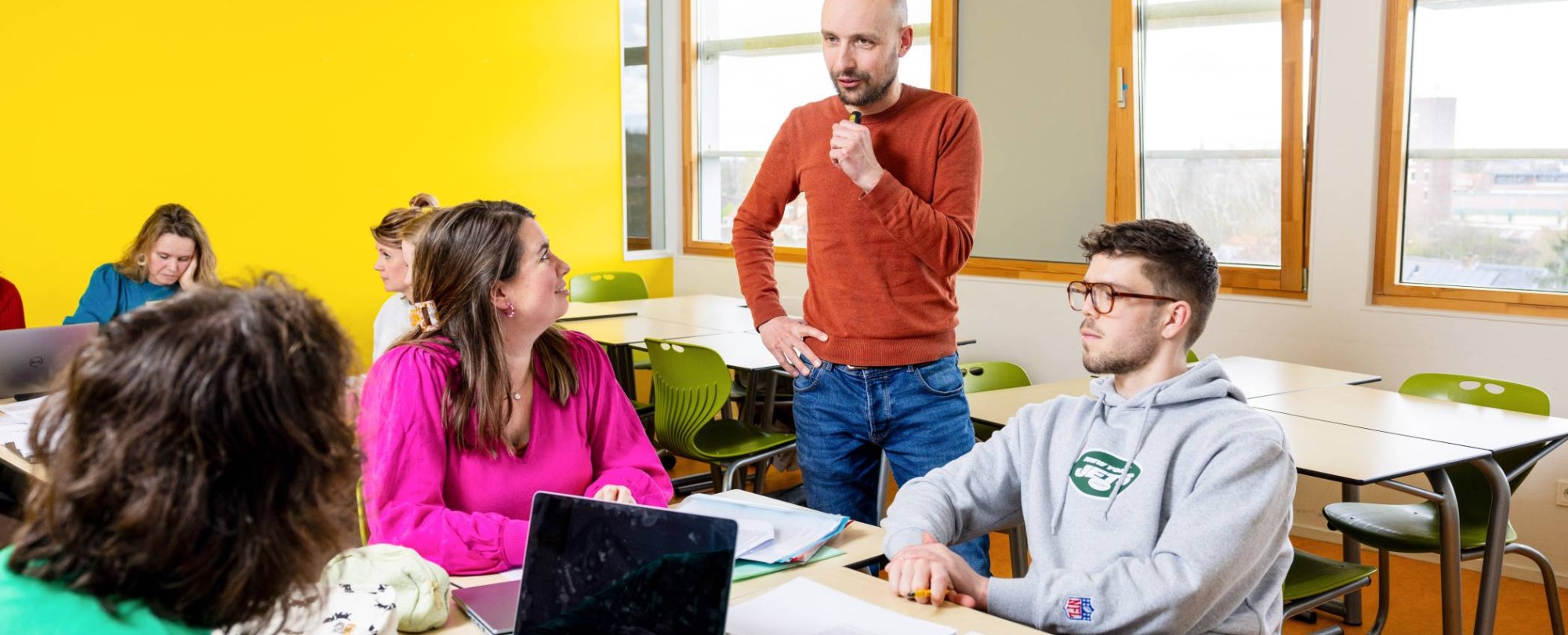 Lachende docent zit aan tafel bij haar studenten.