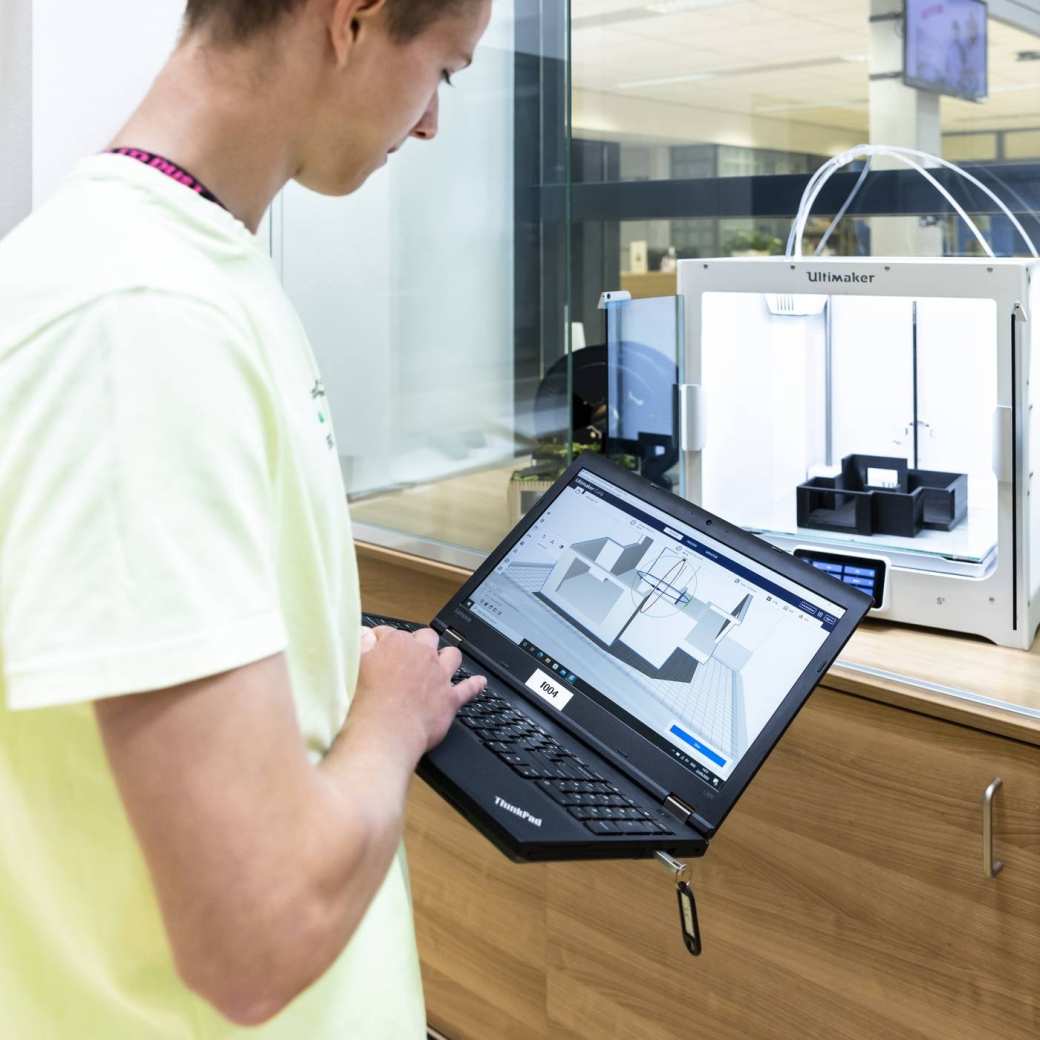 student geeft via een notebook instructie aan een 3d printer