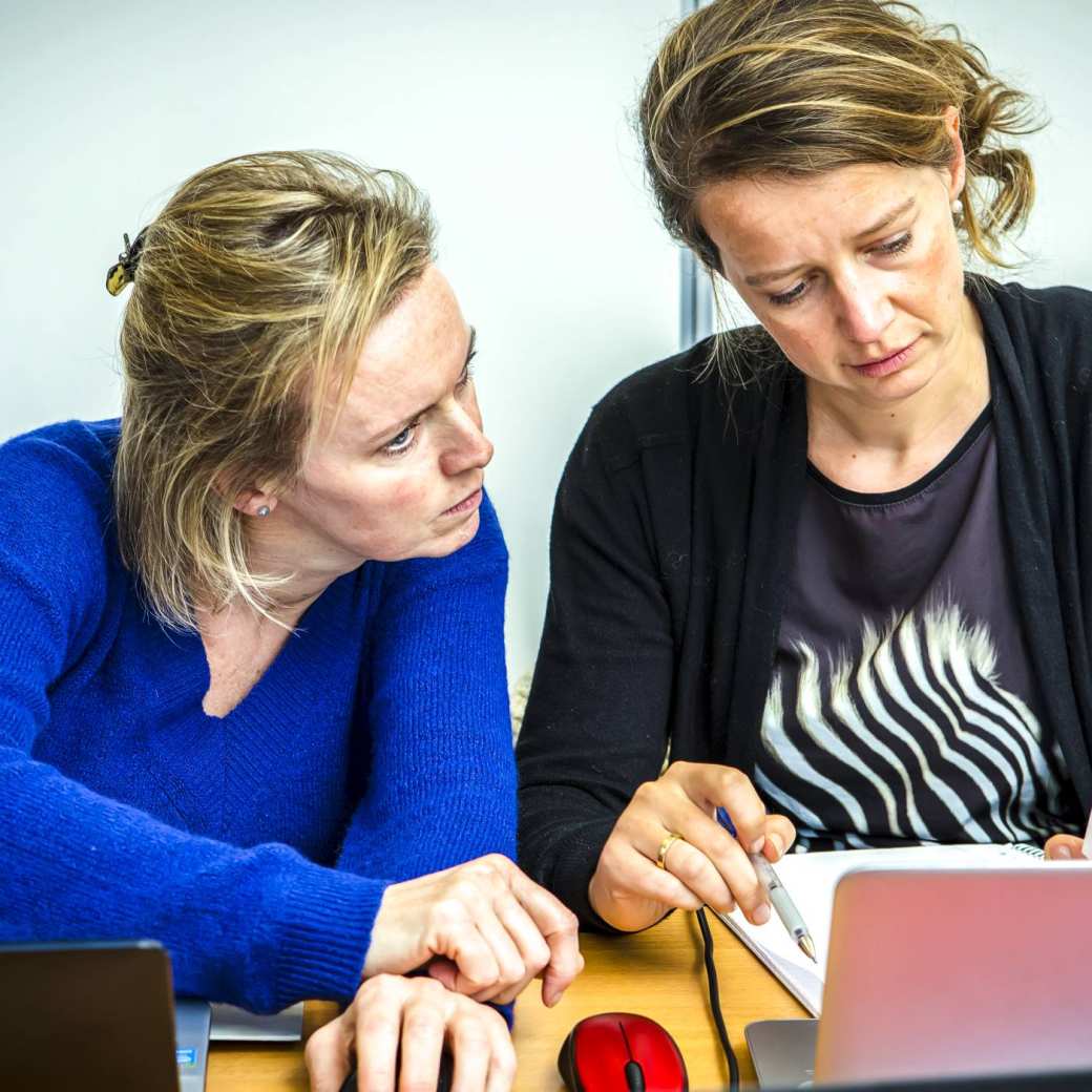 Twee zorgmedewerkers kijken samen op een laptop terwijl ze overleggen.