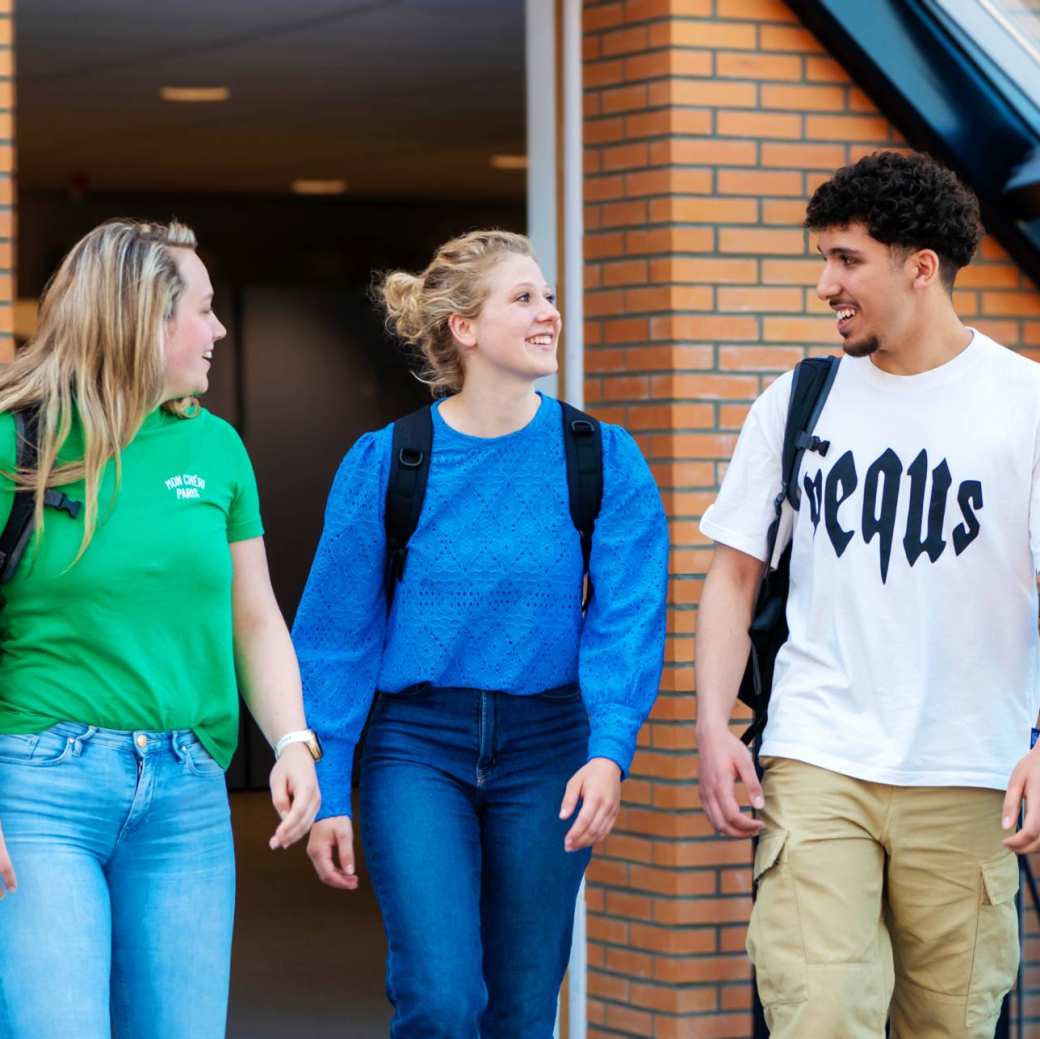 3 studenten lopen vrolijk over de brug met rugzak