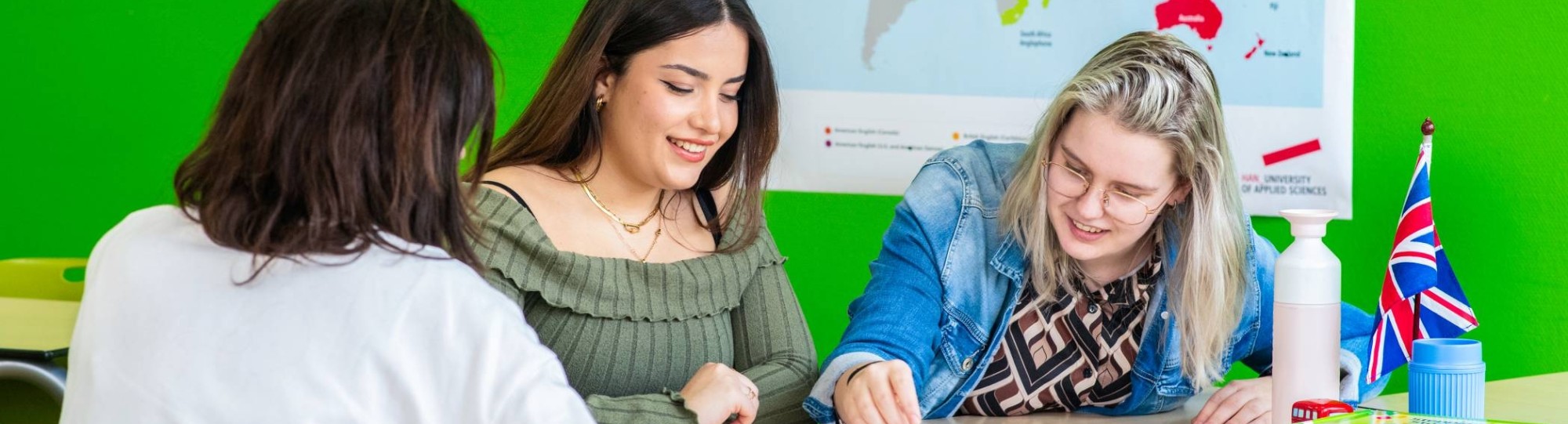 Drie studenten spelen in een lokaal waar de Engelse vlag hangt 'Mens, erger je niet!'
