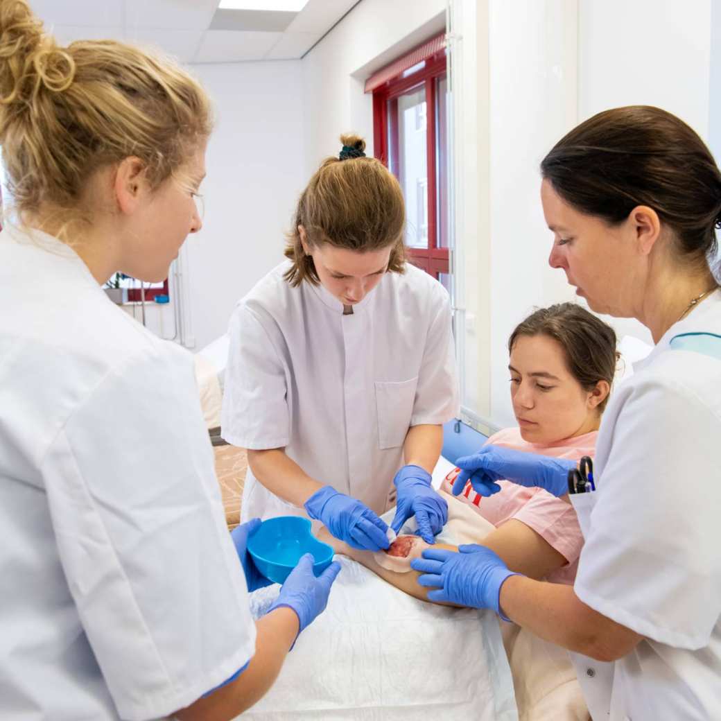 Student Verpleegkunde zwachtelt een voet onder supervisie van een docent in een praktijklokaal