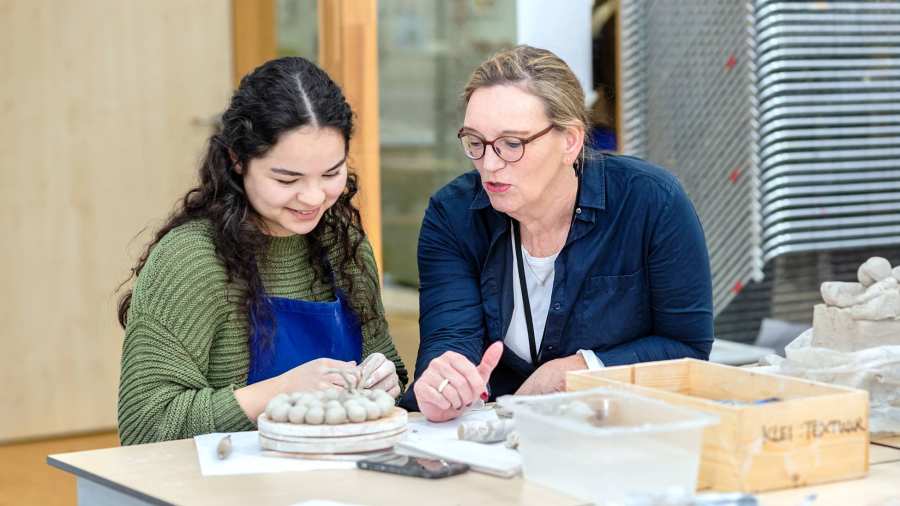 Fotoshoot maakdagen beeldende vorming 2022. Docent met studente tijdens les beeldende vorming. Helpt met kleien.