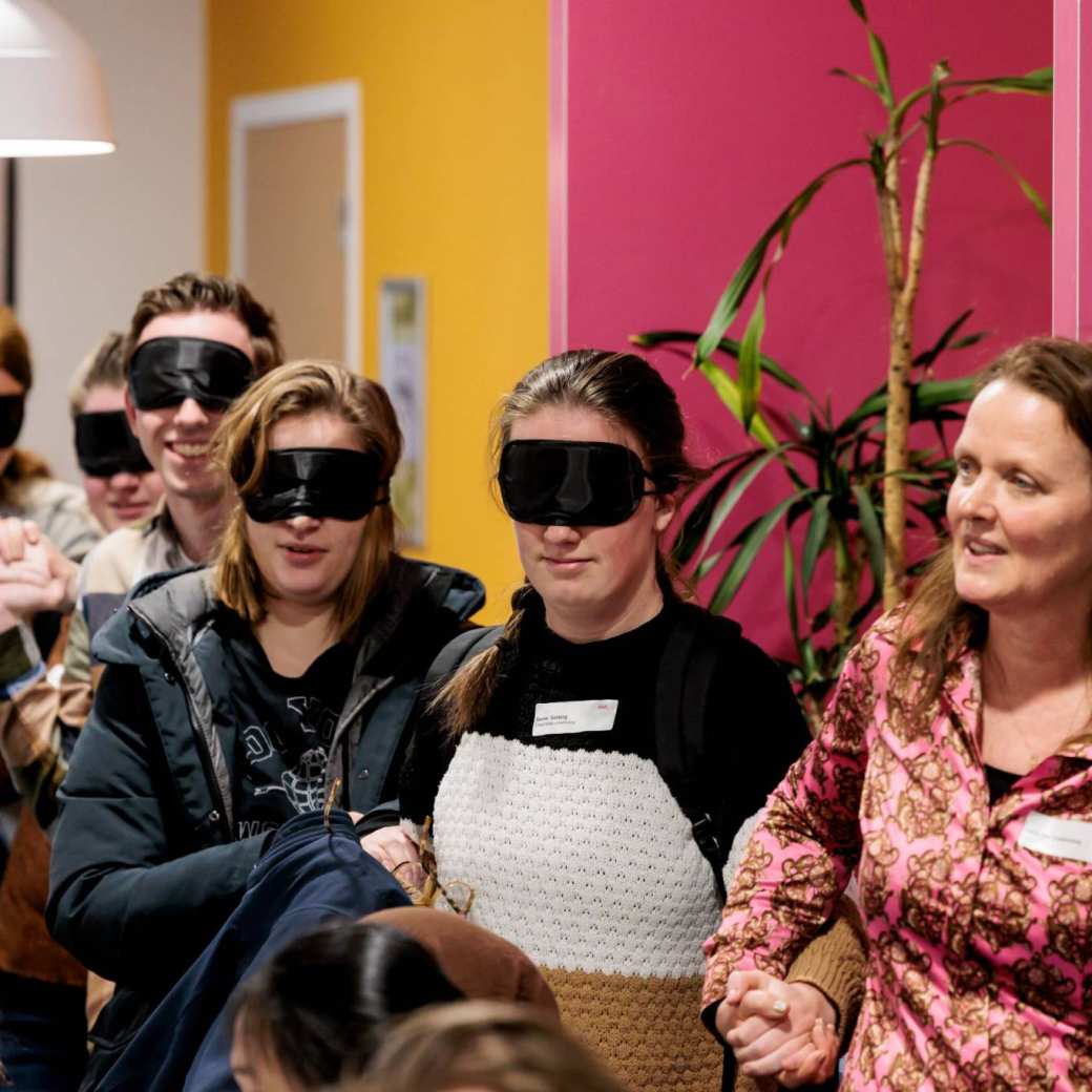 Iemand van de organisatie van het festival LOS begeleid geblinddoekte deelnemers naar een tafel