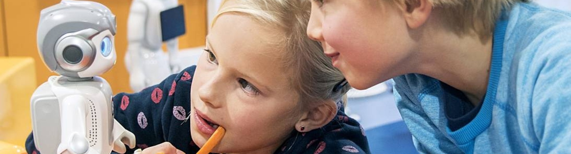 jongen en meisje met pen in mond kijken naar kleine zorgrobot tijdens iXbites event