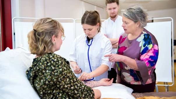 Docent geeft uitleg aan 3 studenten tijdens bloeddruk meten