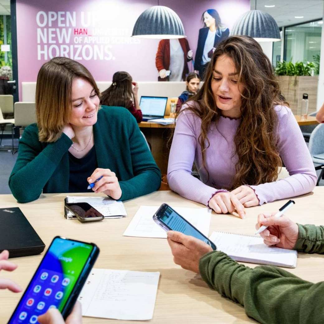 drie studenten ad bedrijfskunde kijken met elkaar mee op laptop in klaslokaal