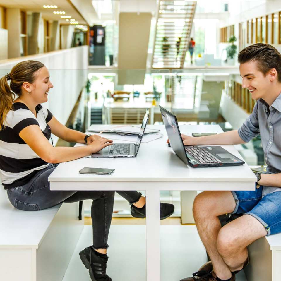 Jongen en meisje studeren samen op laptop in grote hal