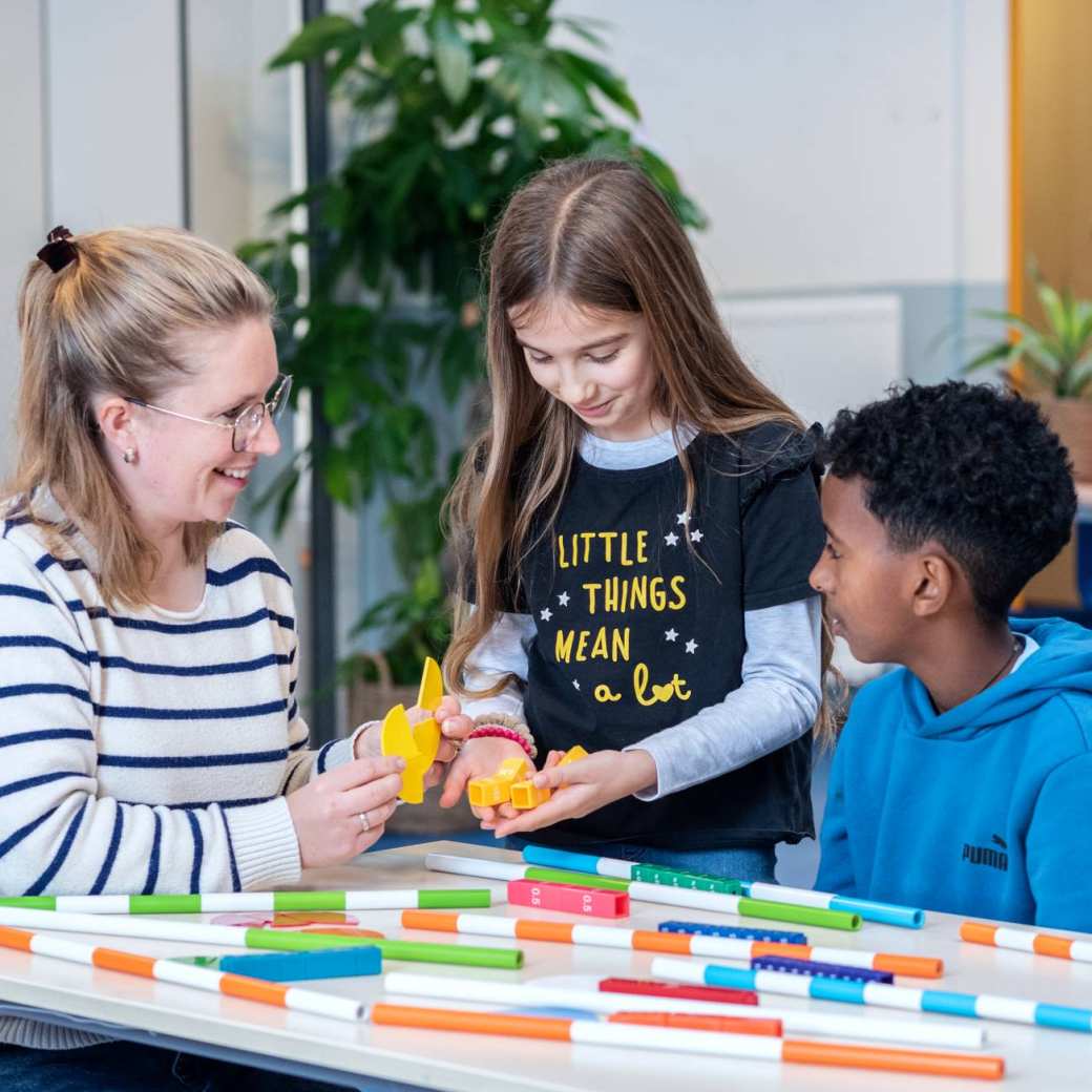 Docente luistert naar haar drie studenten die aan de tafel zitten te overleggen.