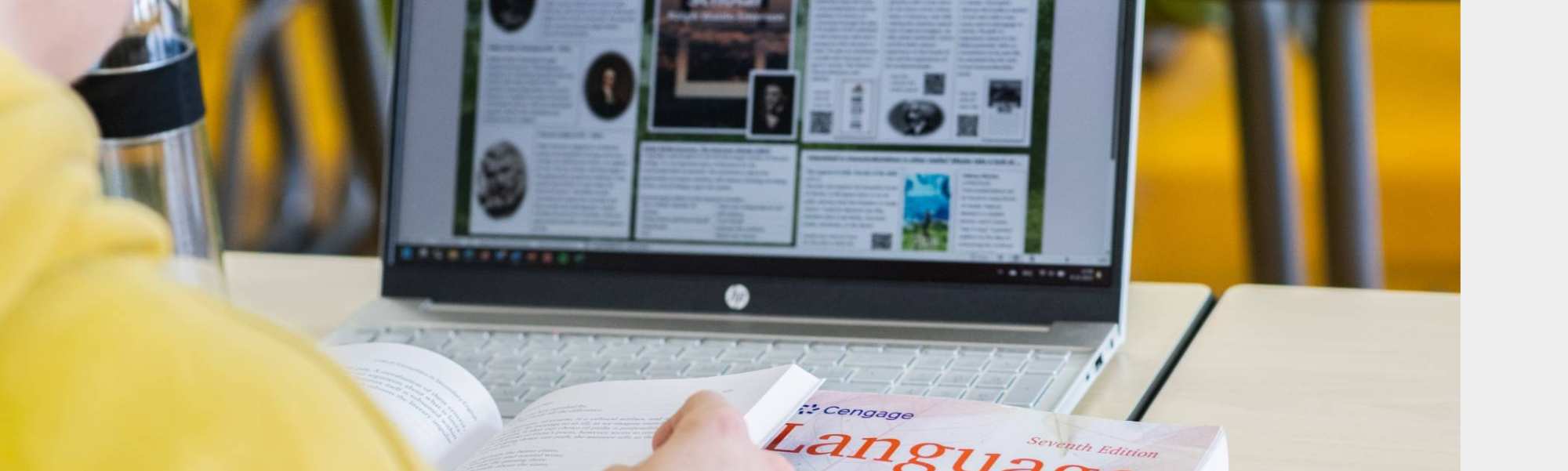 Foto Master Academie Educatie. Een masterstudent zit achter haar laptop met een boek opengeslagen in haar handen. 