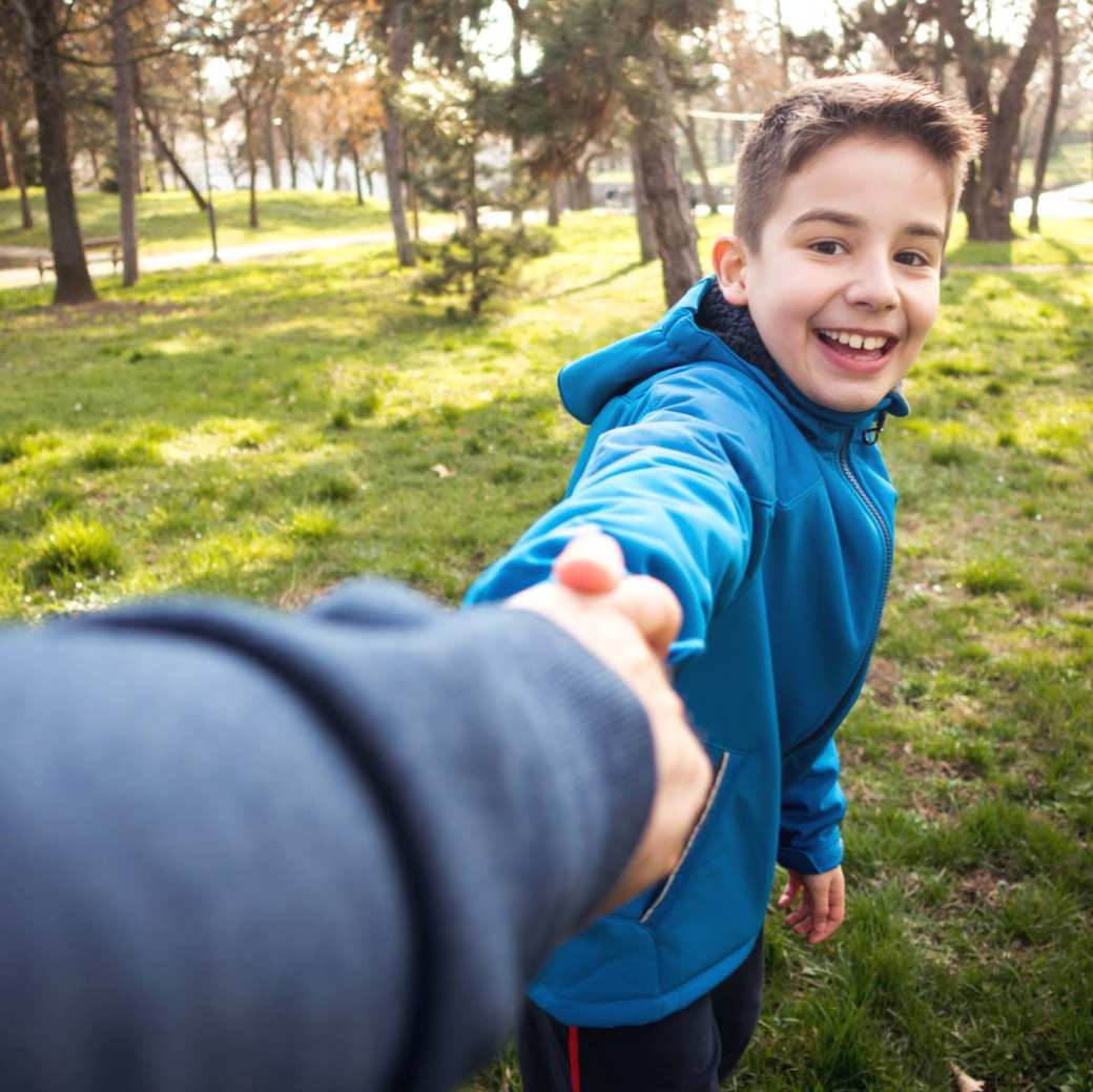 jongen in park die hand van ouder vasthoudt