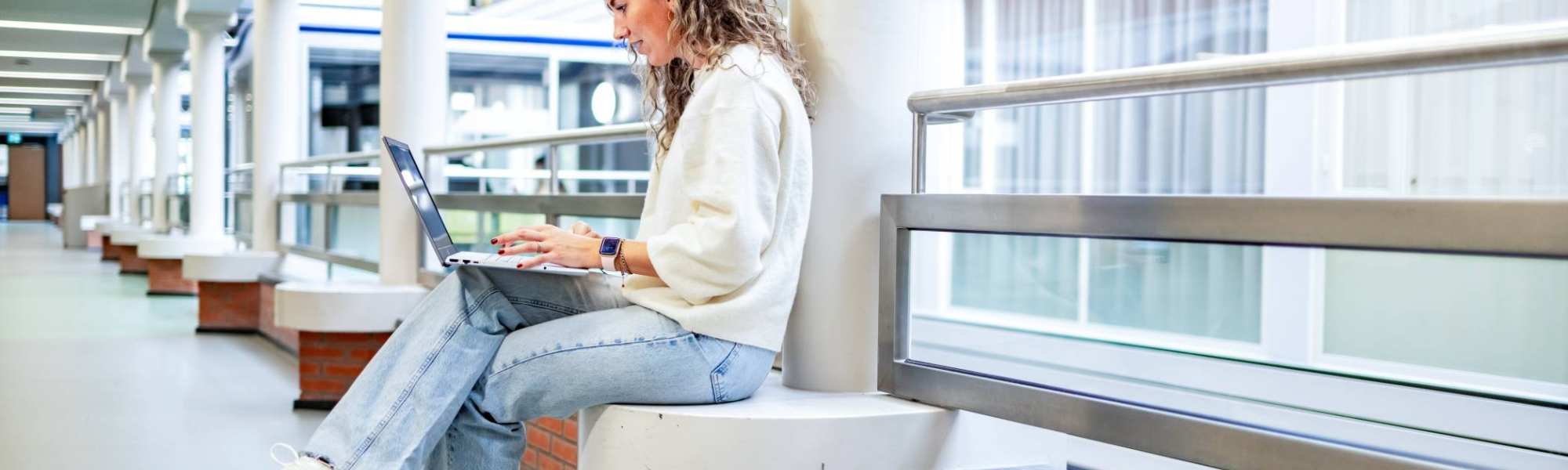 Student van de bachelor Commerciële Economie deeltijd, duaal in gang met laptop. 