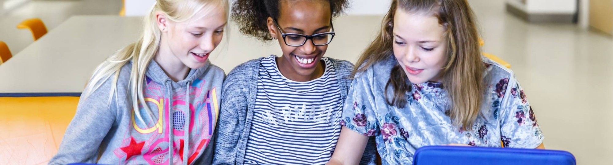 Drie kinderen zitten op een rijtje achter hun laptop met blauwe hoes.